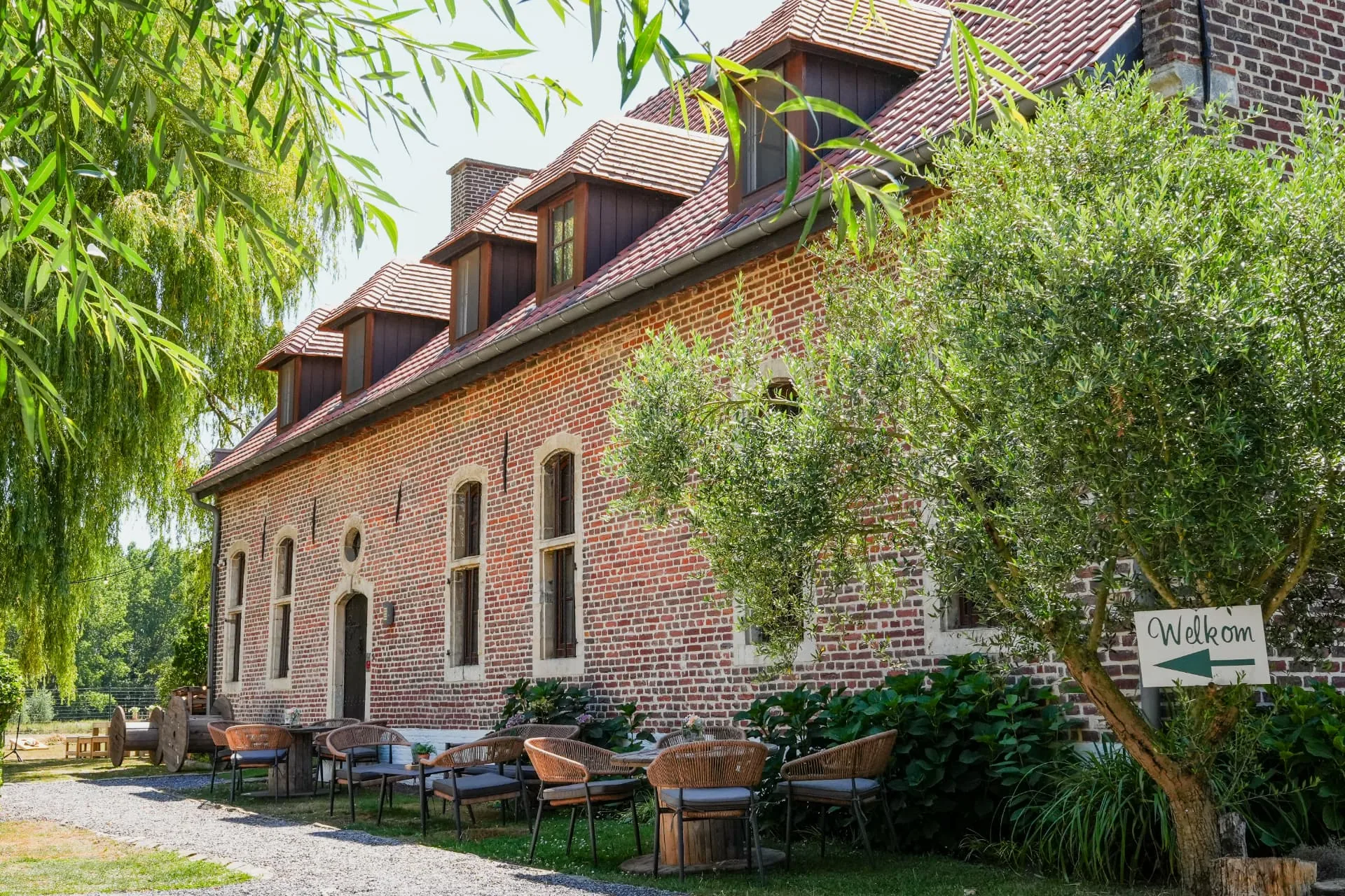 Bakstenen hoeve met terras, olijfboom en welkomstbord bij Huis van Mem